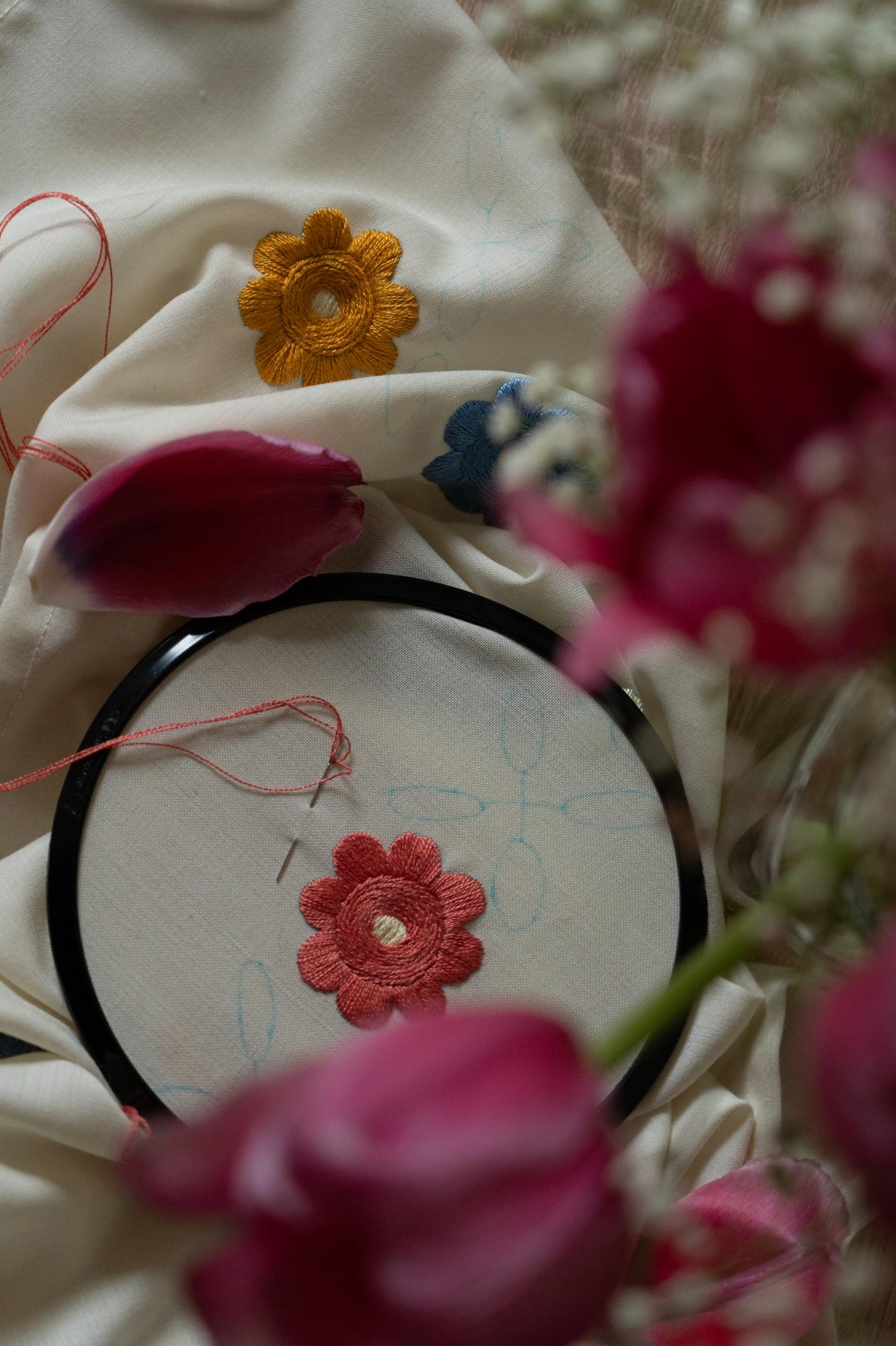 Mano che ricama un dettaglio floreale su tela di lino